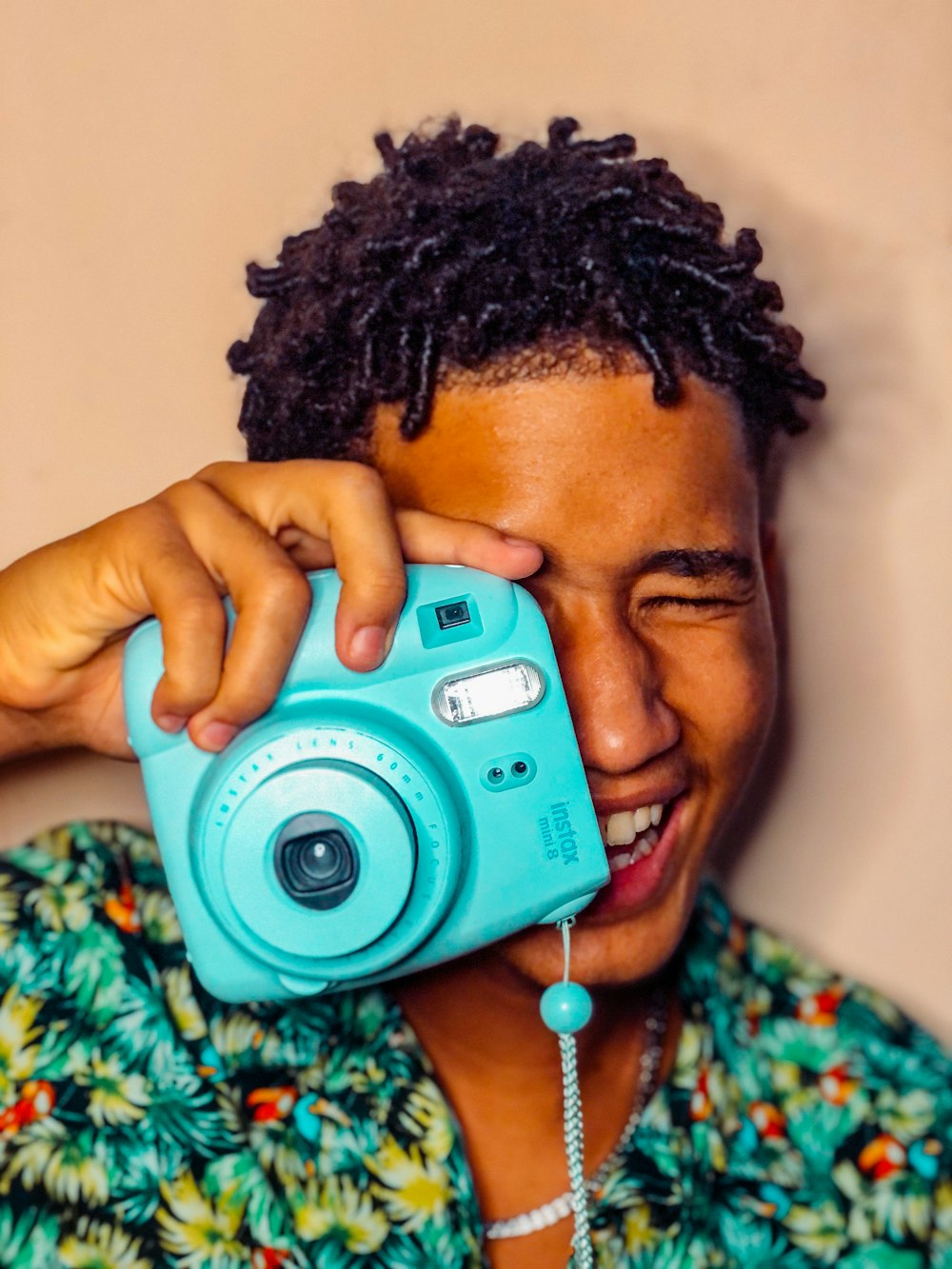 woman in green and yellow floral shirt holding pink and silver camera