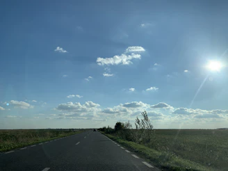 An open road stretching into the horizon under a bright blue sky with scattered clouds.