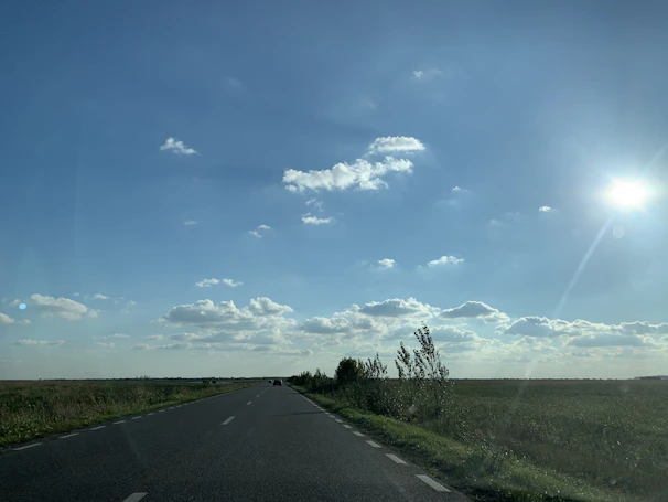 An open road stretching into the horizon under a bright blue sky with scattered clouds.
