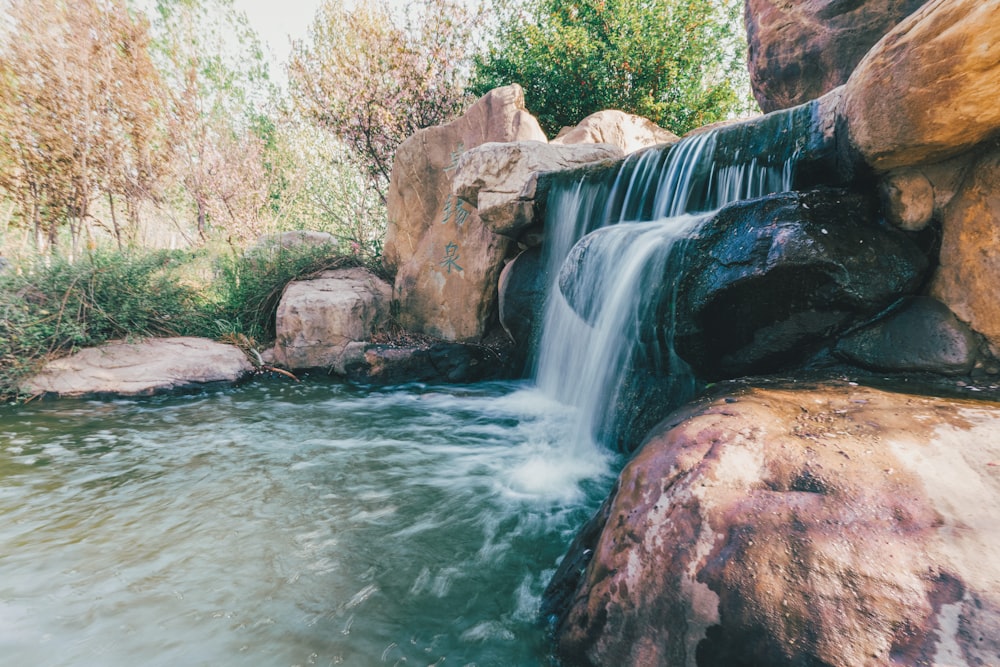 water falls between brown rocks and green trees during daytime