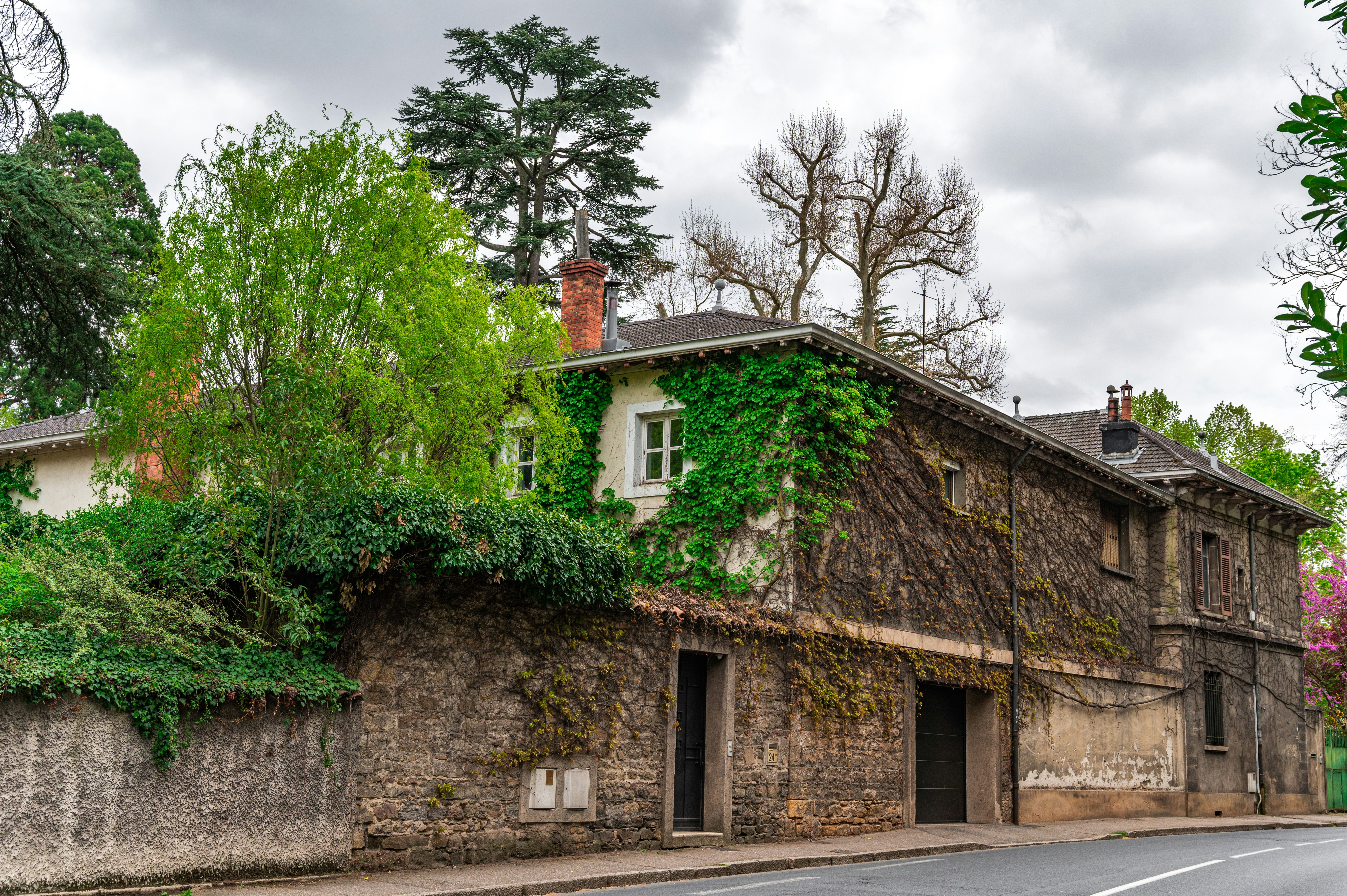 brown concrete house near green trees under white clouds during daytime