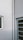 A corner of a building featuring a white drainpipe running vertically along the wall. There is a small, square window with closed blinds on the left and a door with horizontal glass panels on the right side. The walls are painted in off-white, and there are visible cracks on the surface.