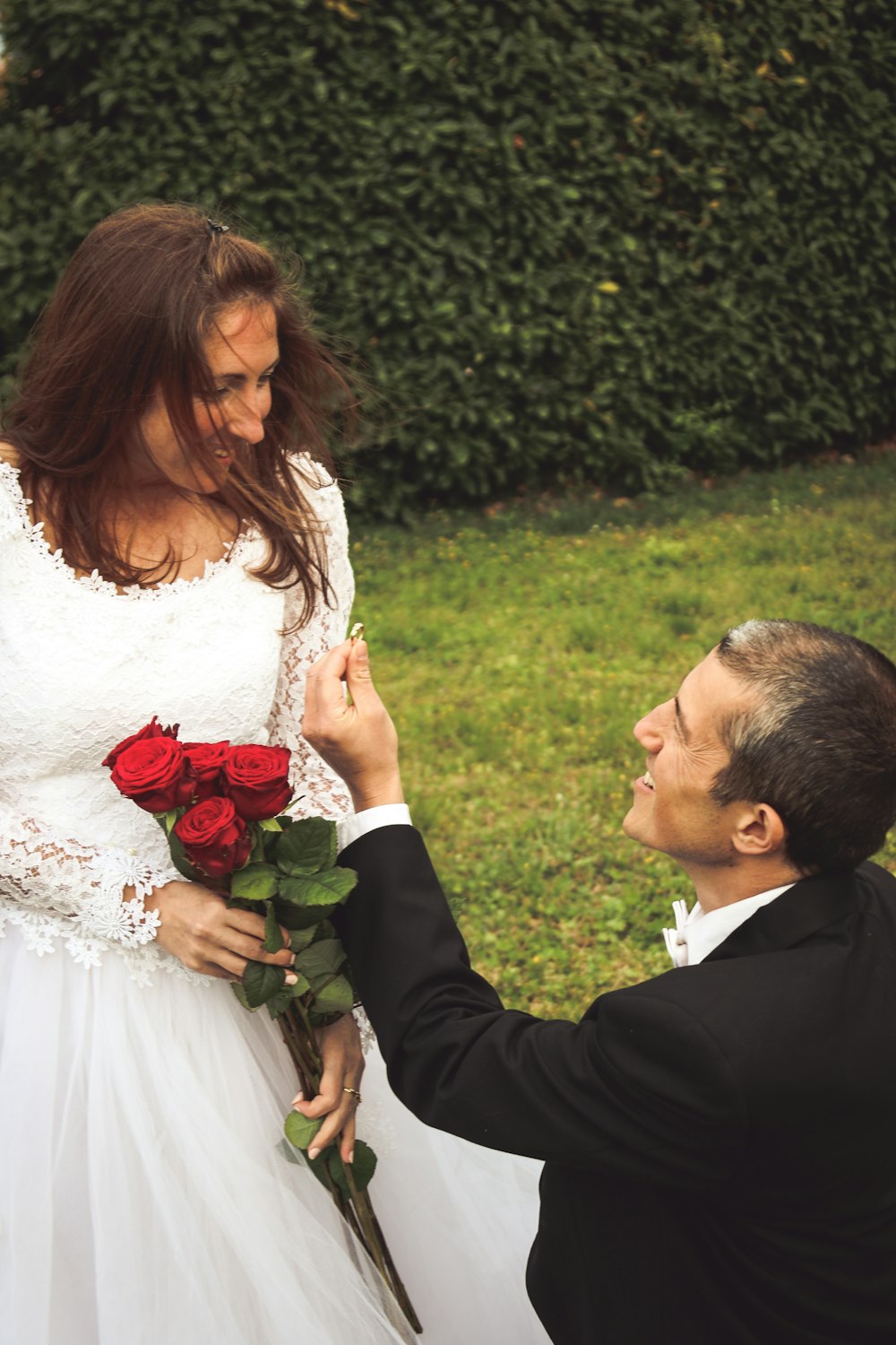 woman in white wedding dress holding red rose bouquet