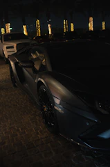 A sleek luxury car parked against Dubai’s night skyline, illuminated by city lights.