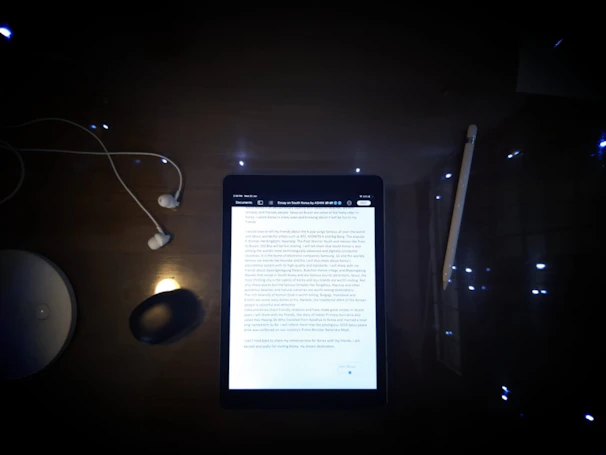 A stylish wireless headset resting on a wooden desk beside a tablet.
