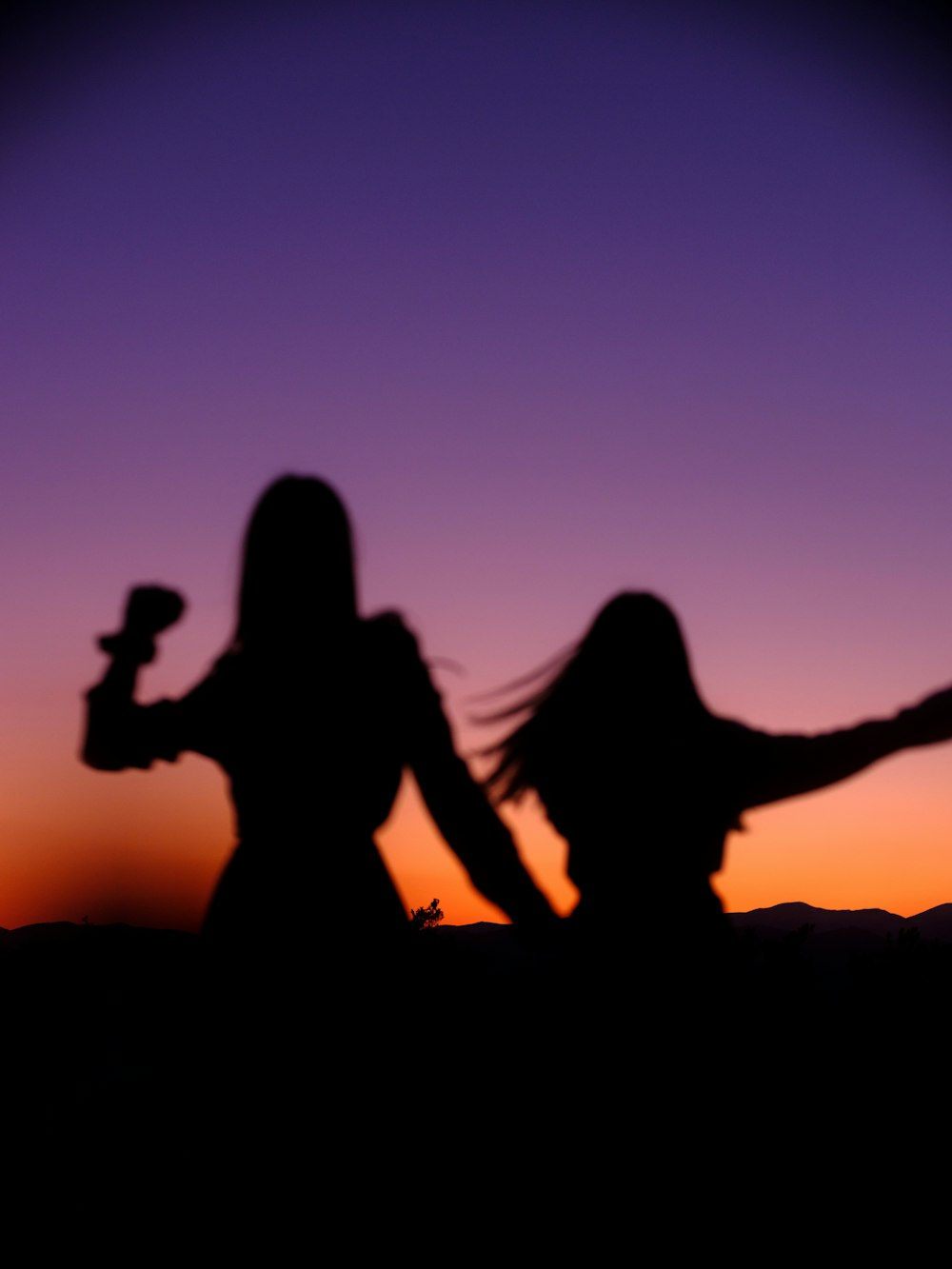 silhouette of 2 women sitting on rock during sunset