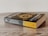 A paperback book titled 'The Fellowship of the Ring' by J.R.R. Tolkien is placed on a wooden surface. The cover features an intricate design with gold elements and text.
