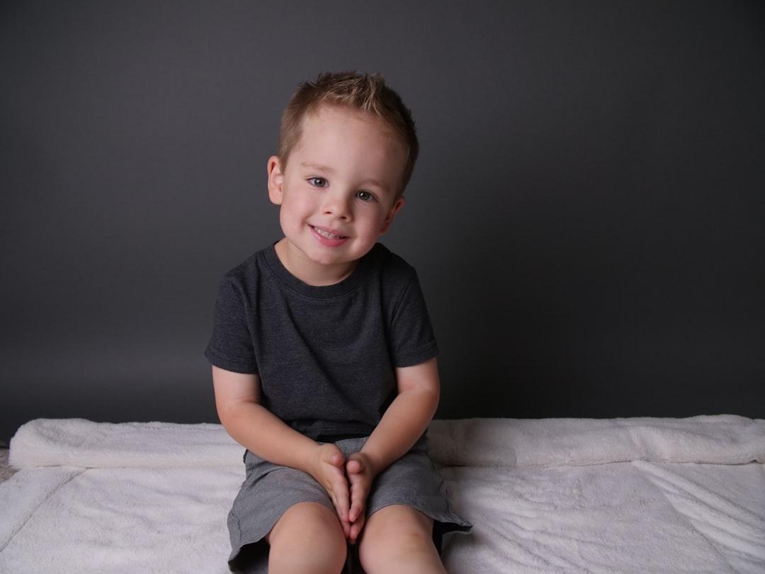boy in black crew neck t-shirt sitting on white bed,