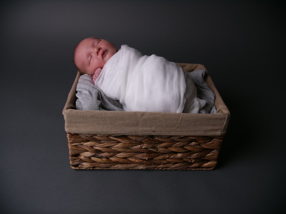 baby in white blanket in brown woven basket