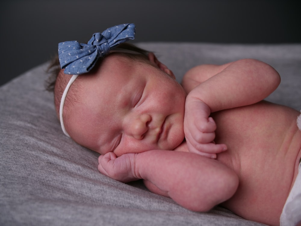 bébé en bandeau bleu et blanc couché sur textile blanc