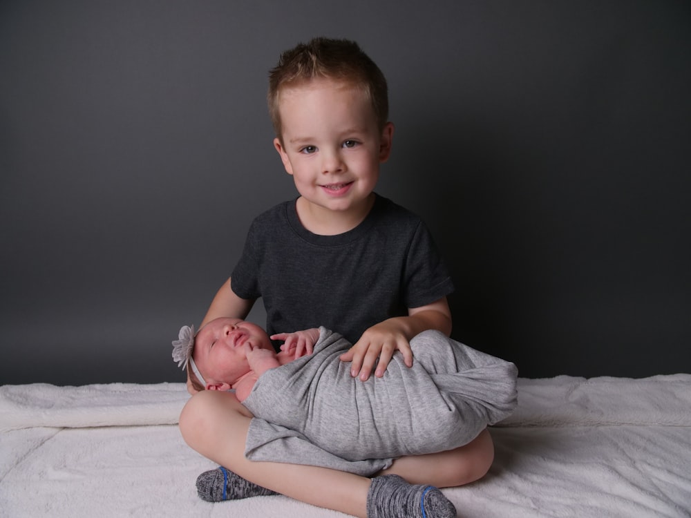 boy in black crew neck t-shirt and gray pants sitting on white textile