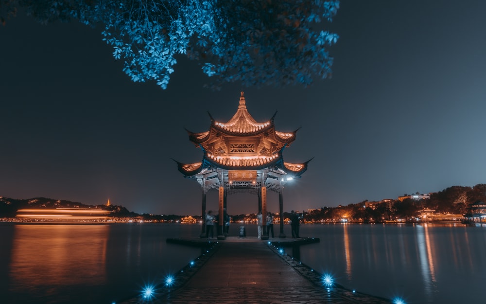 Gazebo de madera marrón cerca del cuerpo de agua durante la noche