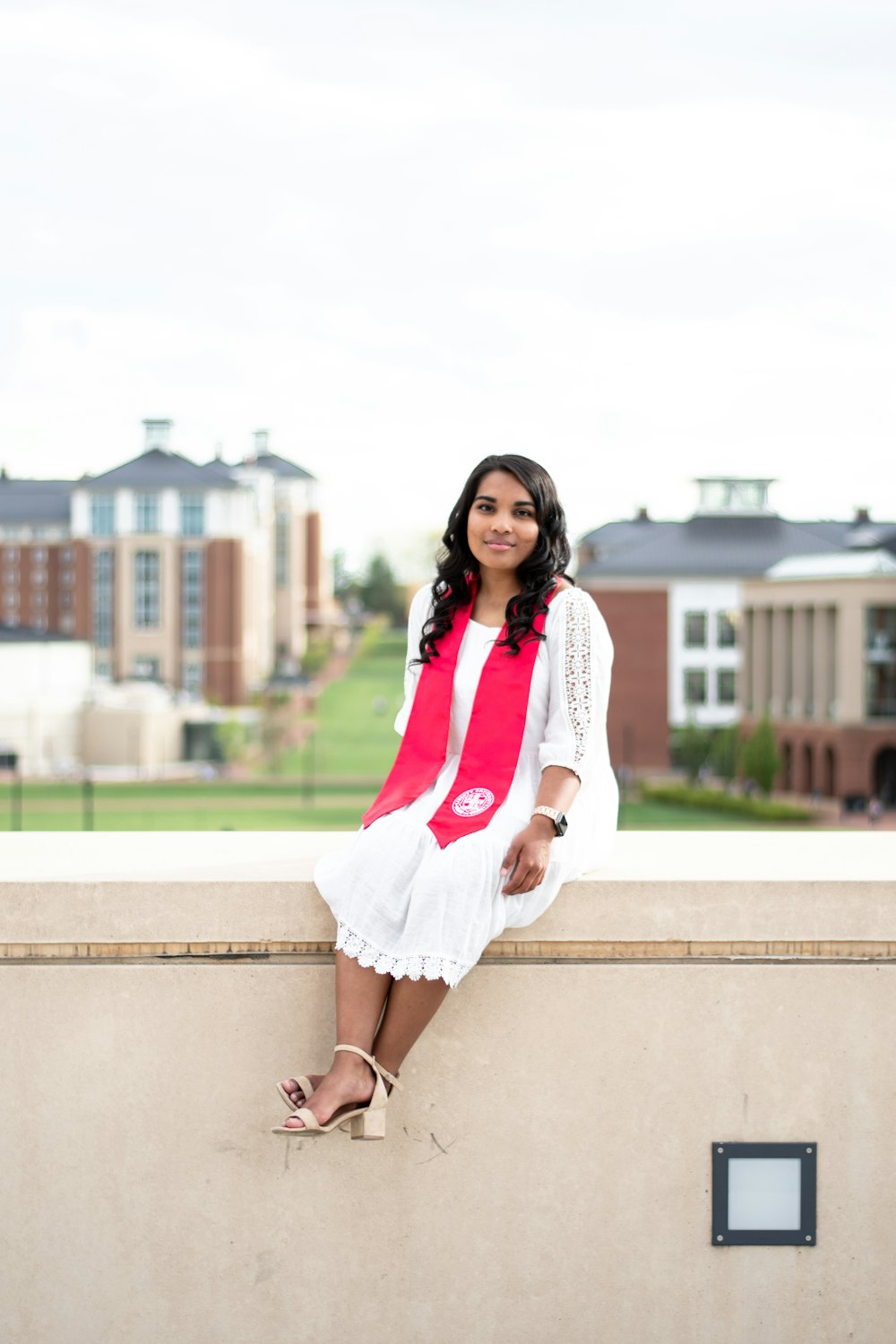 woman in white long sleeve dress and red scarf standing on concrete wall during daytime