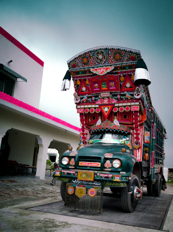 A colorful truck art-inspired delivery van parked outside a traditional Pakistani neighborhood.