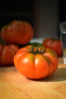 Close-up of ripe heirloom tomatoes glistening with morning dew on a rustic wooden table.
