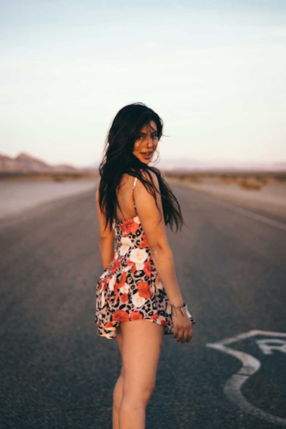 woman in white red and black floral dress standing on gray asphalt road during daytime