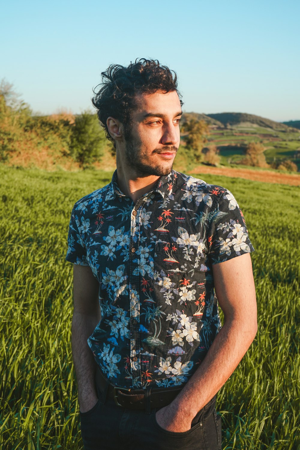 man in blue and white floral button up shirt standing on green grass field during daytime