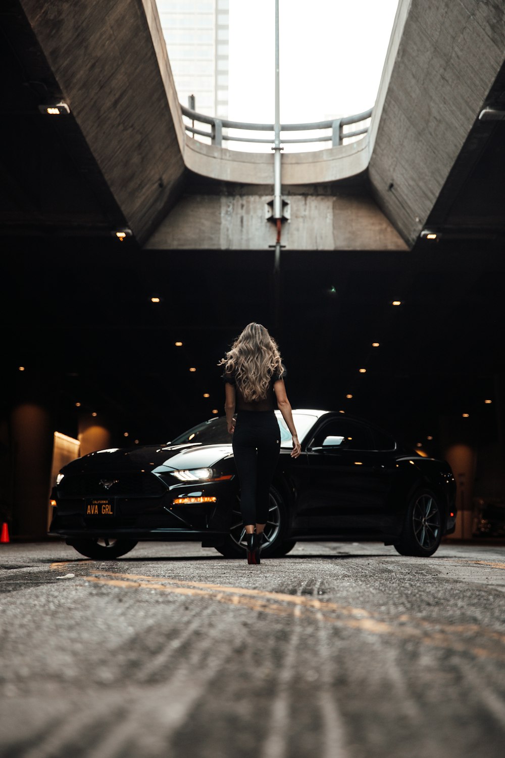 woman in black tank top standing beside black sedan