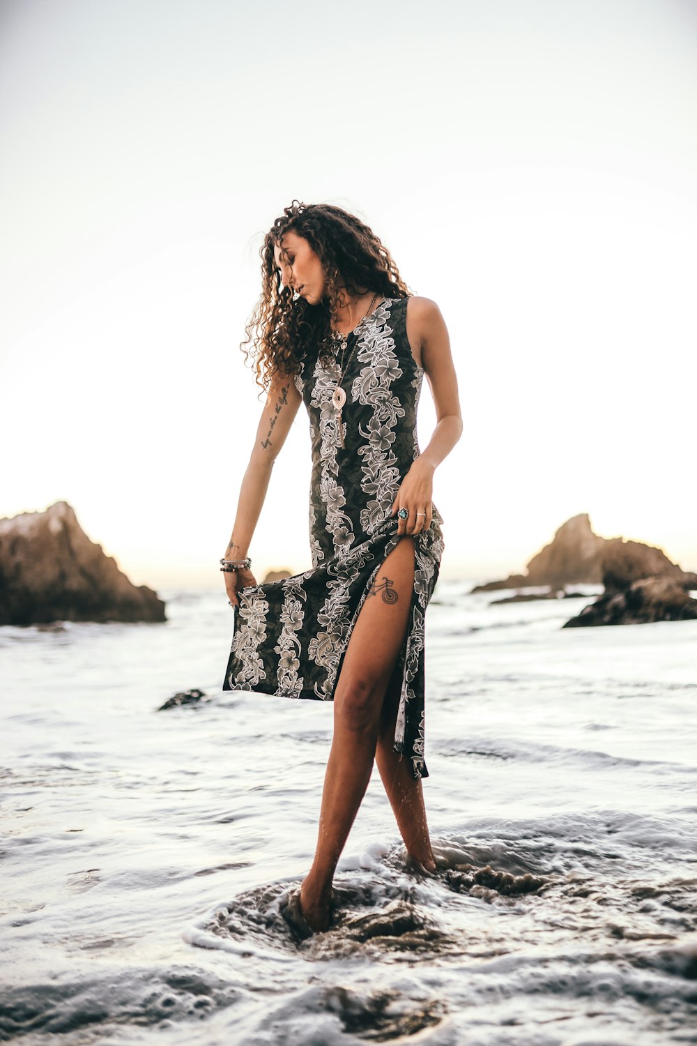 woman in black and white floral sleeveless dress standing on beach during daytime