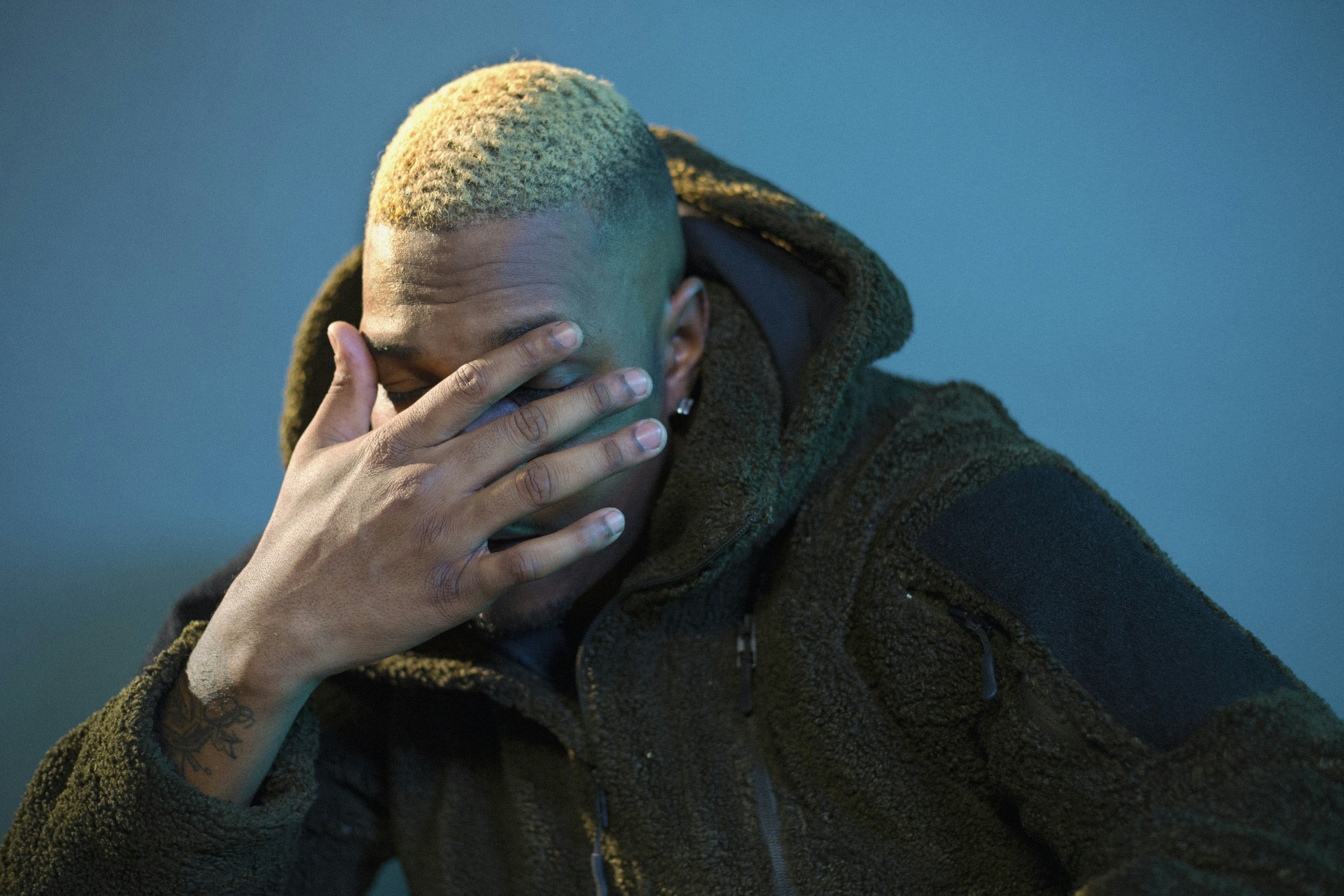 man in black jacket covering his face with his hand