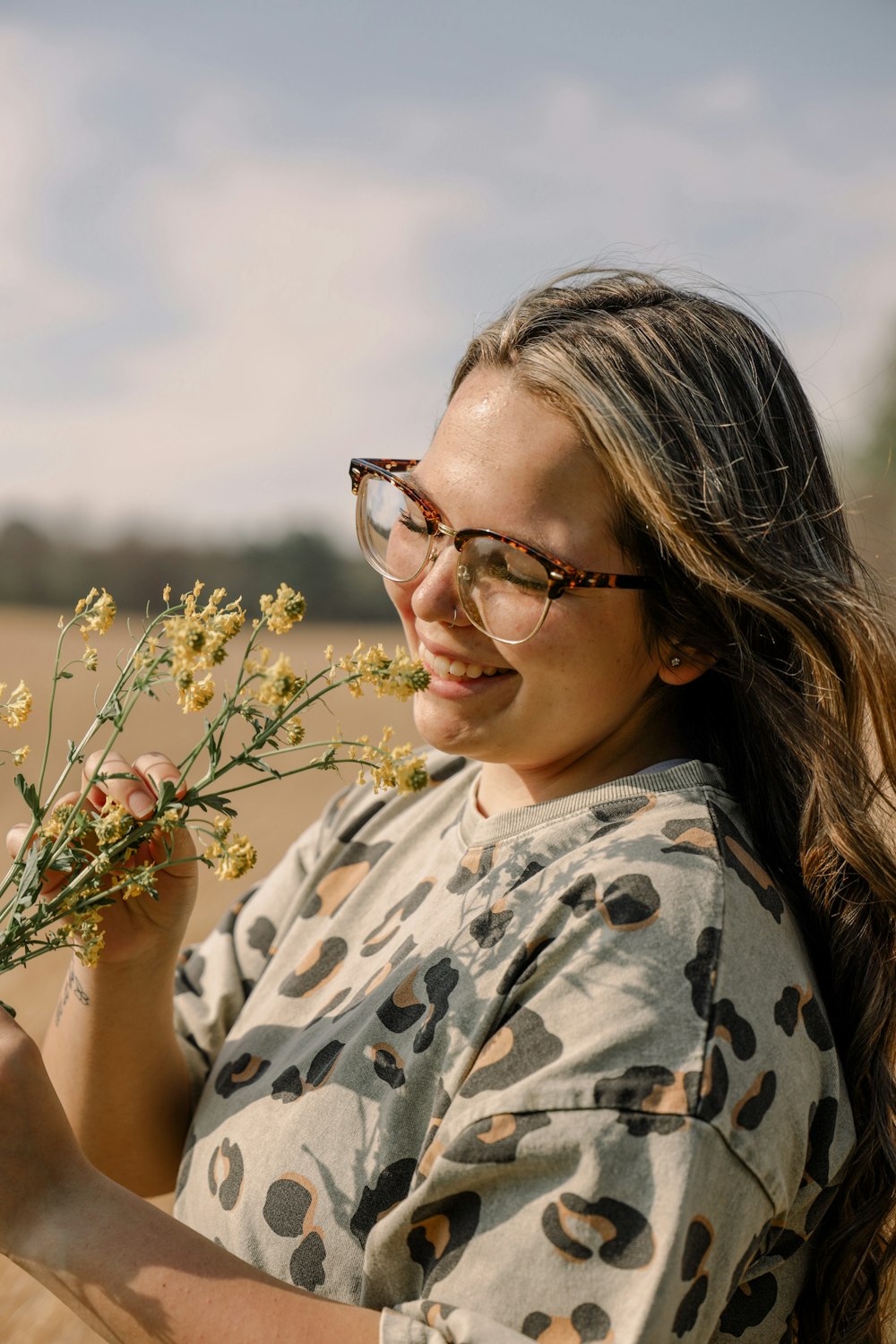 woman in black framed eyeglasses and white and black floral shirt holding yellow flower during daytime