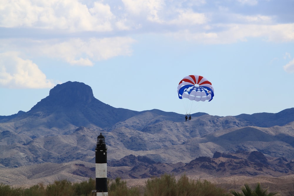 pessoa em vermelho branco e paraquedas azul sobre a montanha durante o dia