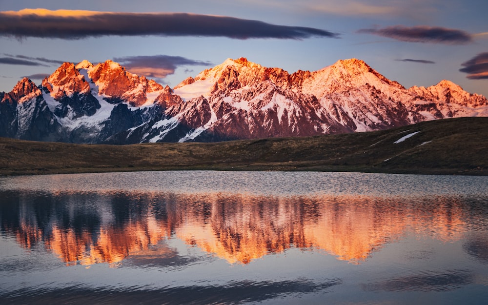 montagna marrone e bianca vicino al lago sotto il cielo grigio