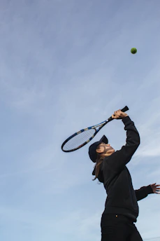 A relaxed tennis player swinging a racket with a soft, flowing motion on a sunny court.