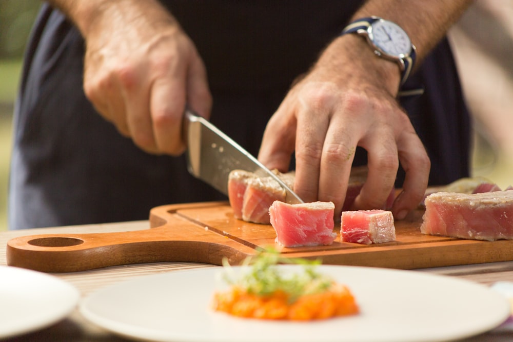 person slicing raw meat on chopping board