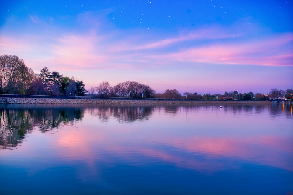 corpo d'acqua vicino agli alberi sotto il cielo blu durante il giorno