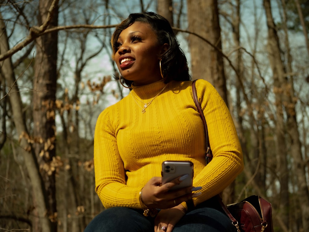 woman in yellow sweater holding black smartphone