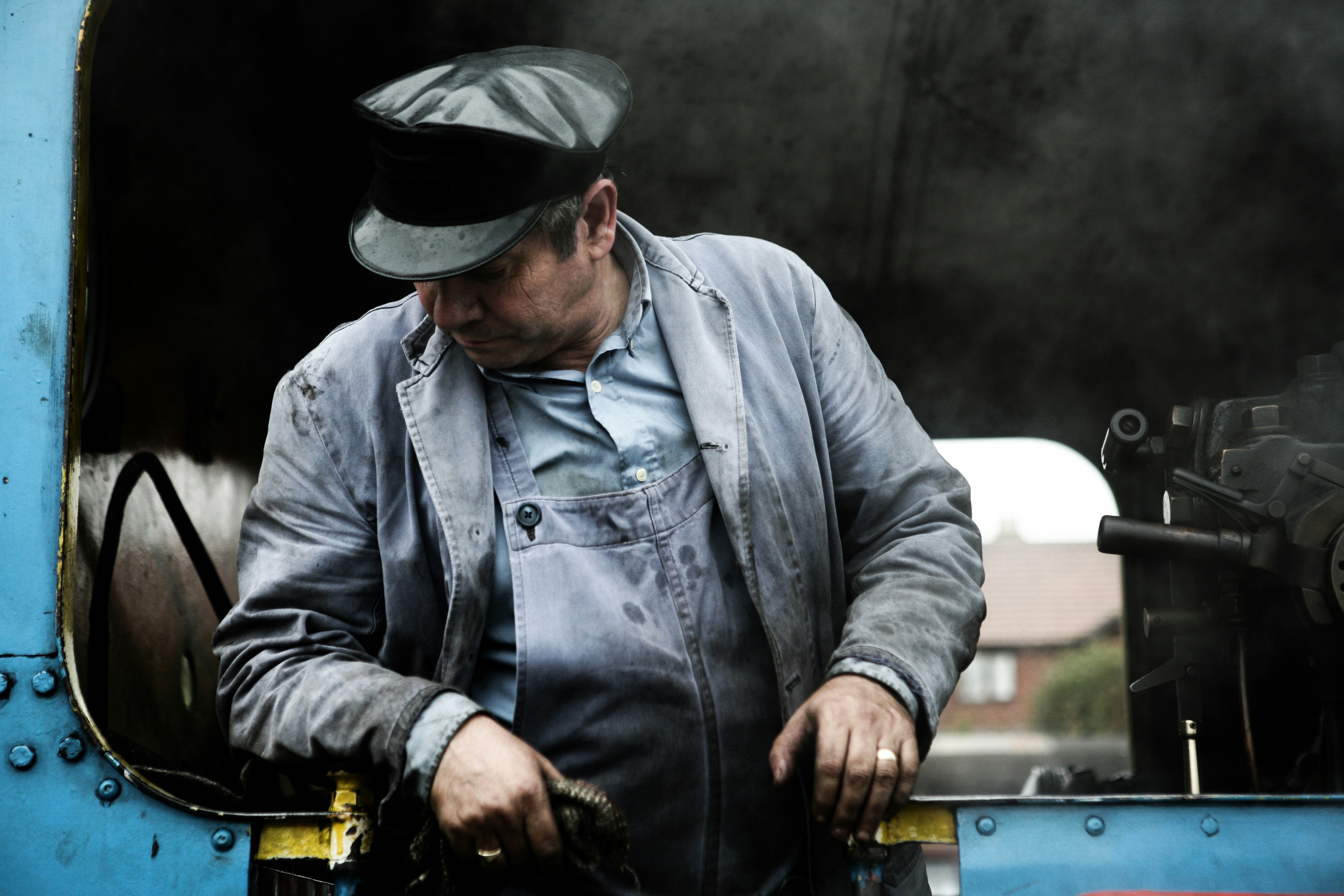 Homme en veste en jean grise et chapeau noir tenant un chien à poil court noir et marron