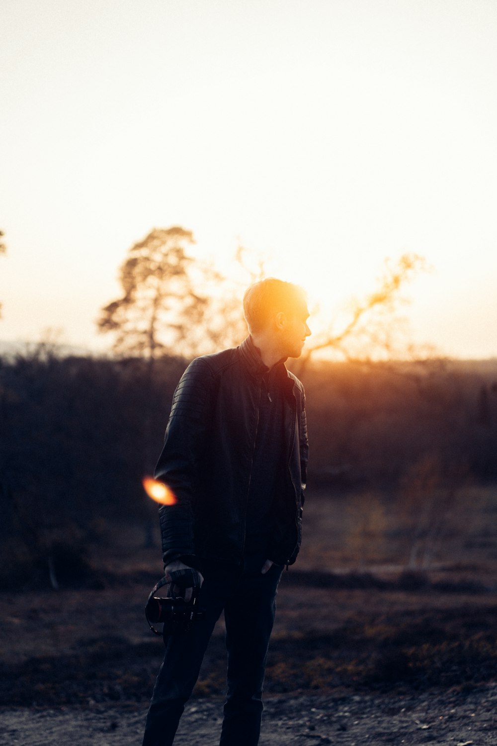 man in black jacket standing on grass field during sunset