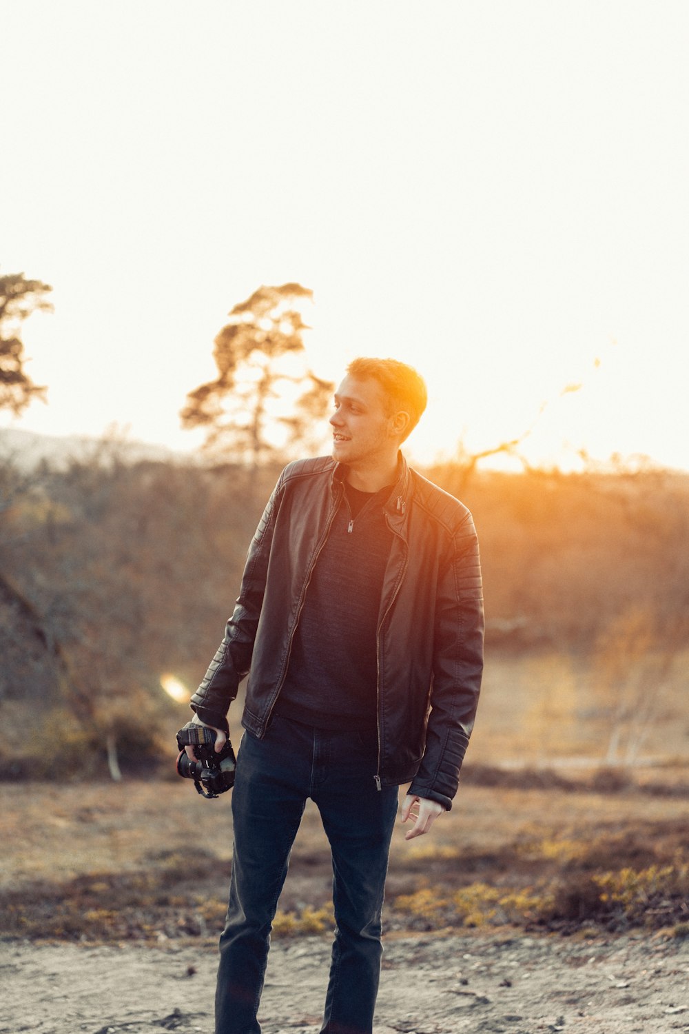 man in black leather jacket and black pants standing on brown field during daytime