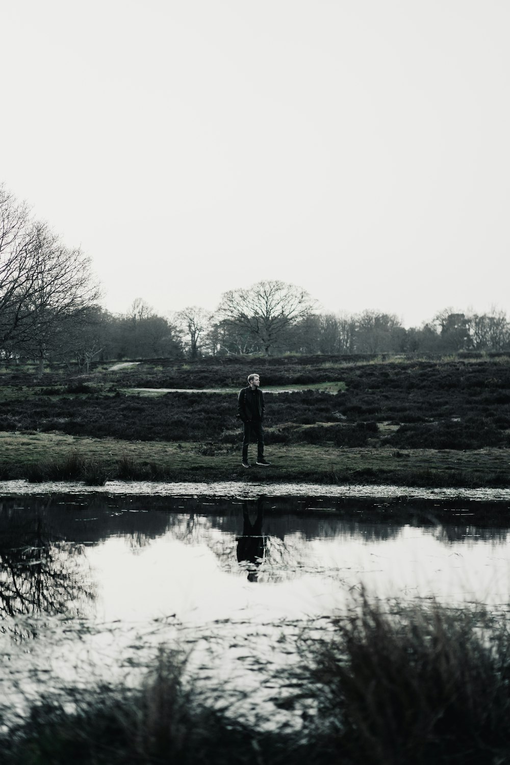 man standing on green grass field near lake during daytime