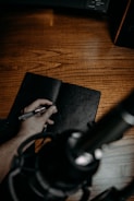 A close-up of hands holding a journal and pen on a wooden table.