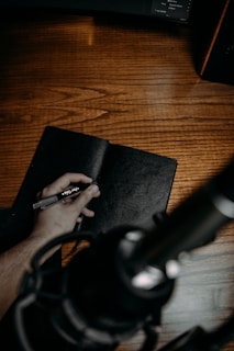 Close-up of hands holding a journal and pen on a wooden table.