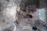 A kaleidoscopic image with a pattern resembling fragmented triangular and diamond shapes. The space is filled with reflections and distorted images, likely involving multiple figures, as well as a window revealing greenery outside.