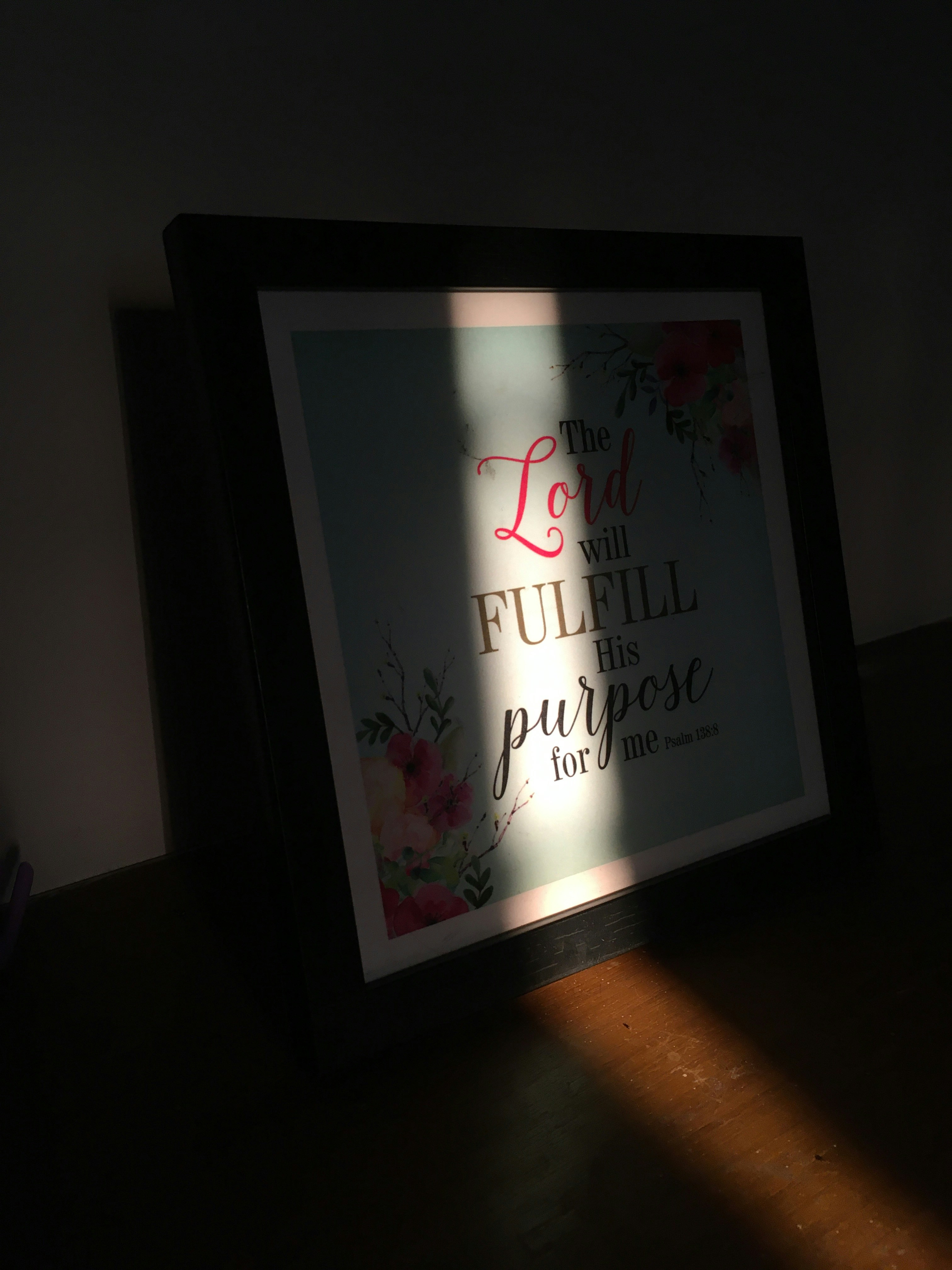 Framed scripture print with elegant hand-lettered text on cream archival paper, warm natural light, minimal white frame on a light plaster wall