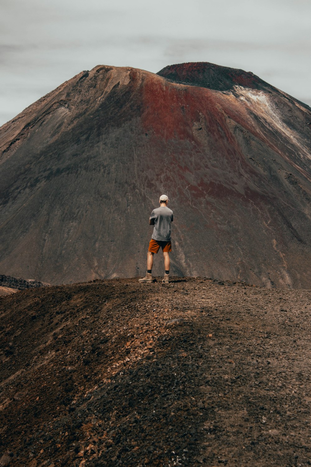 man in white t-shirt and brown shorts standing on brown rocky mountain during daytime