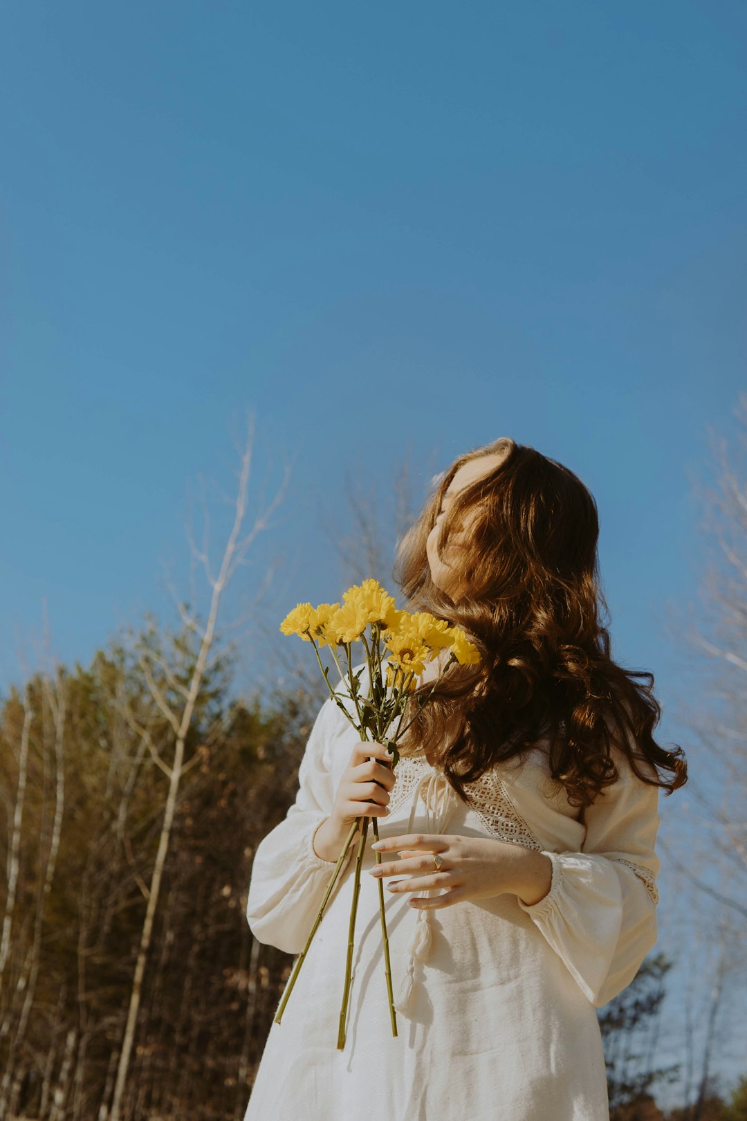 woman in white long sleeve shirt holding yellow flower during daytime