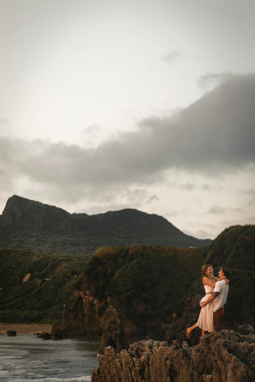 woman in white tank top standing on brown rock formation under white clouds during daytime