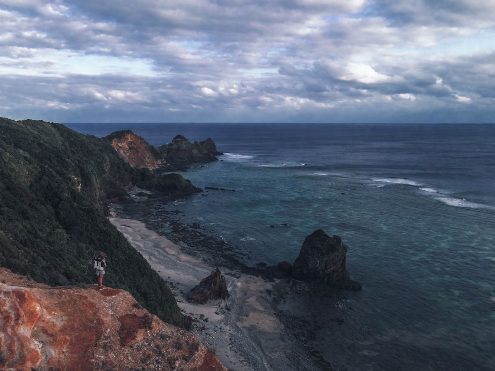 person standing on rock formation near body of water during daytime