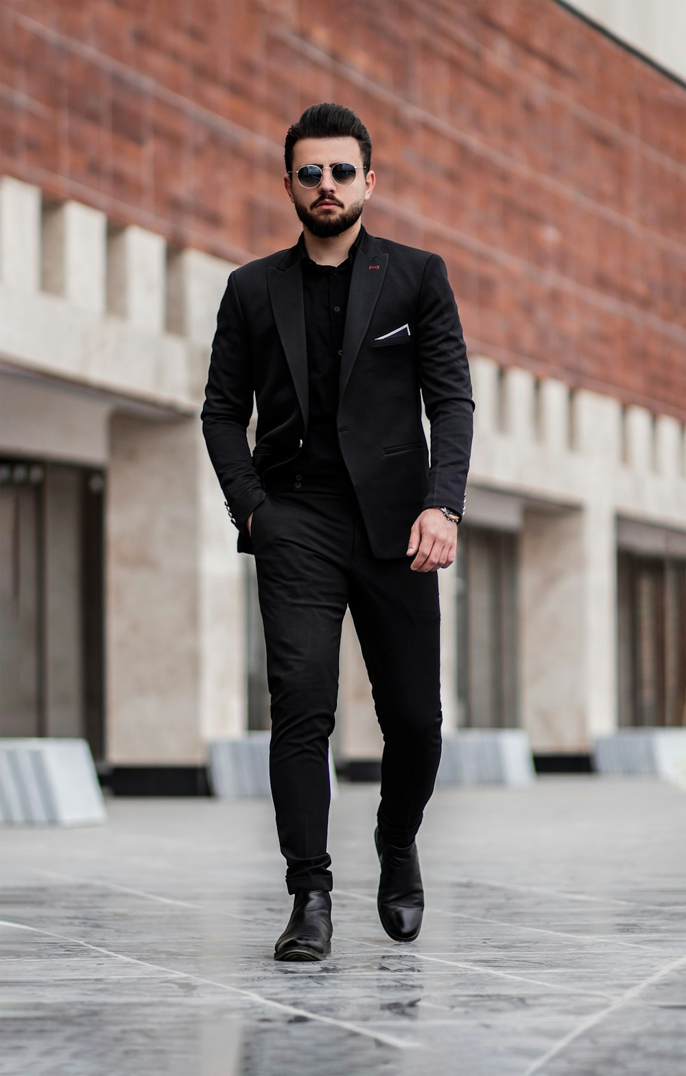 man in black suit jacket and black pants standing on gray concrete ...