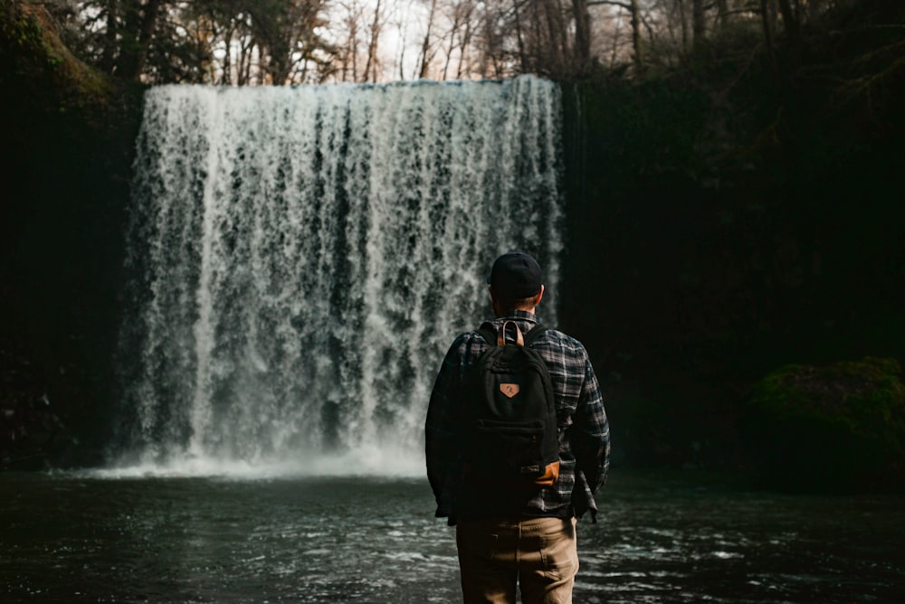 man in black jacket standing in front of waterfalls