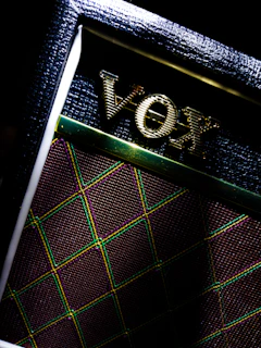 Close-up of a sleek black guitar amplifier with glowing neon green accents in a dark room.