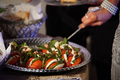 person holding stainless steel fork and knife slicing tomato on black ceramic bowl