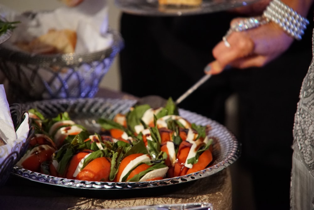 person holding stainless steel fork and knife slicing tomato on black ceramic bowl