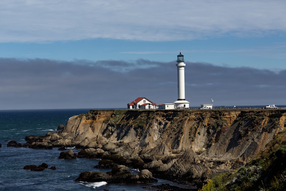 white and red lighthouse on brown rock formation near body of water during daytime