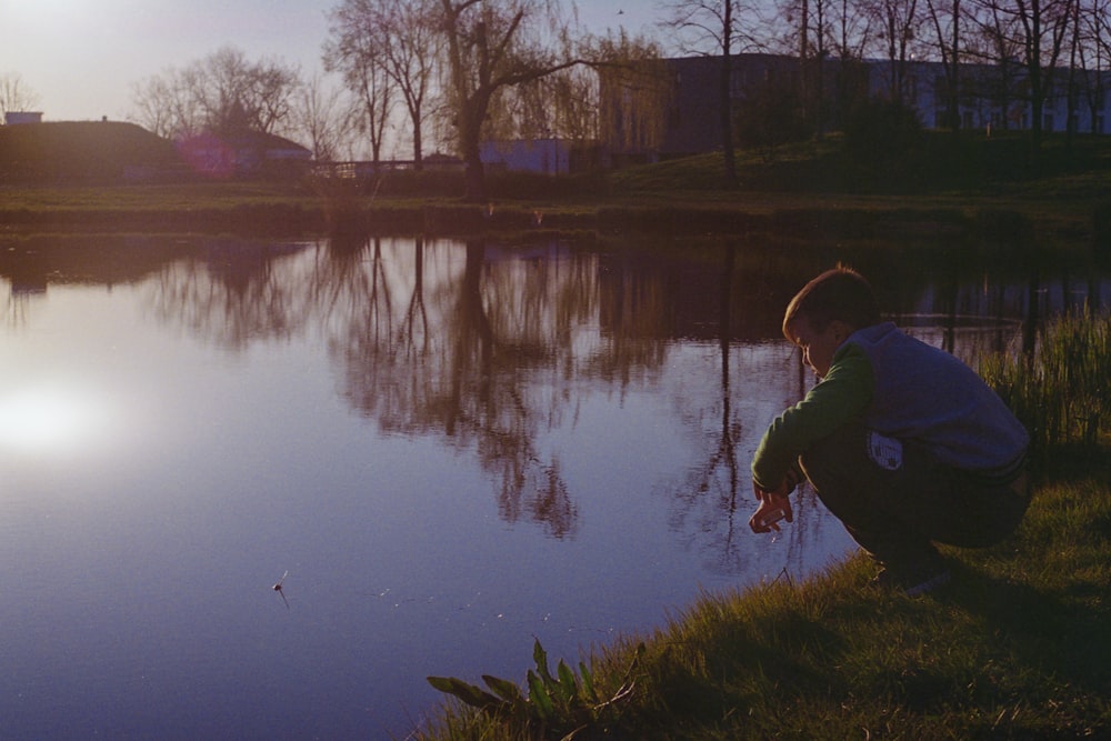 man in blue jacket and black pants standing on green grass field near lake during daytime